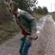 A woman takes a shit on a gravel road in the rain.